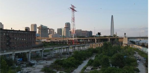 The site today: vacant riverfront land under elevated rail